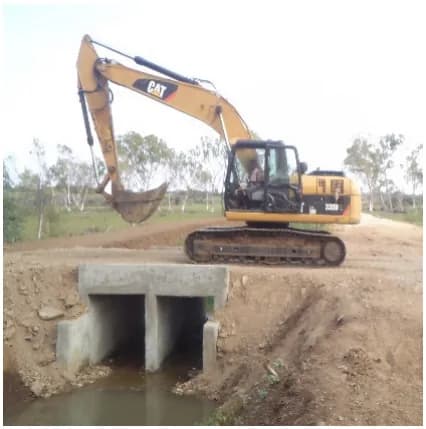 Twin-cell reinforced concrete box culvert installed on a rural road, with a tracked excavator working the embankment